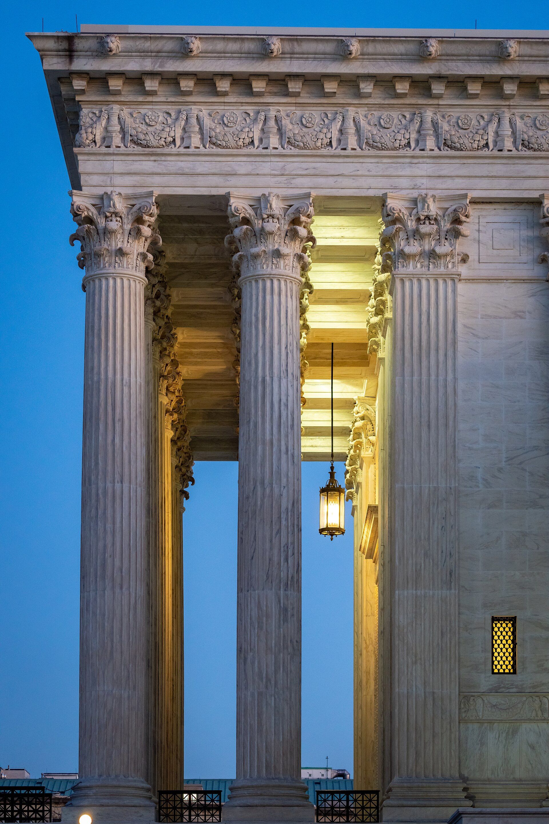 Marble columns of the United States Supreme Court at dusk, with a lantern lit beneath the portico.